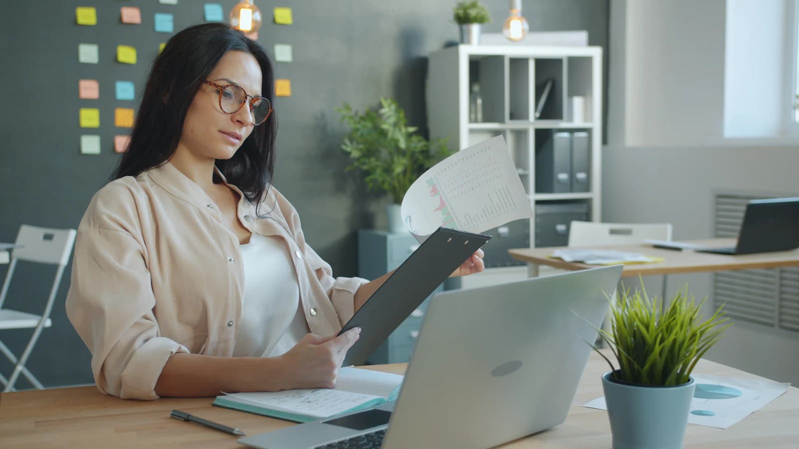 Een vrouw bekijkt documenten aan haar bureau in een lichte werkruimte.